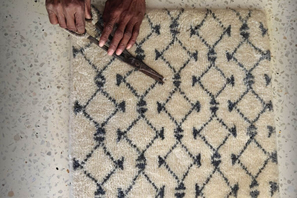 Artisan trimming handmade wool rug sample during finishing process